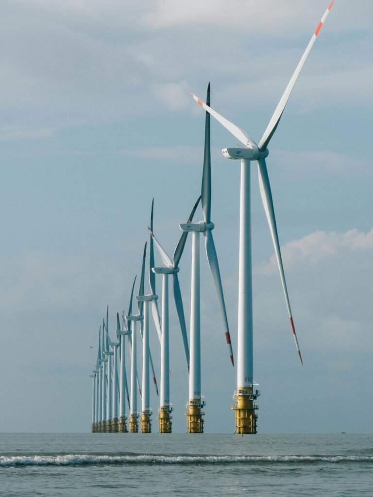 A row of offshore wind turbines in the ocean under a clear blue sky, showcasing renewable energy.